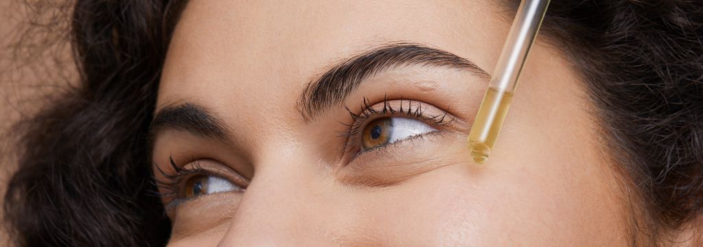Mulher sorridente aplica sérum facial em sua pele do rosto